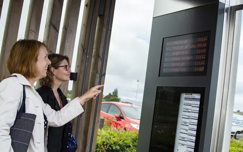 Two women looking at RTI at bus  stop on Inverness Campus